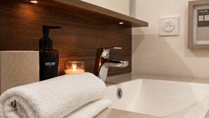 A modern bathroom with a large bathtub, a wooden vanity, a hand soap dispenser, and a lit candle. - Apartment with terrace and private garden near Disney & shopping center  (Bussy-Saint-Georges)