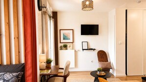 Ein modernes Wohnzimmer mit Holzboden, einem Esstisch, einer Couch, einem an der Wand befestigten Fernseher und einer Deckenleuchte.