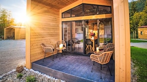 Eine Holzhütte mit überdachter Veranda, Sitzgelegenheiten im Freien und einer Glasdoor, die zum Innenbereich führt.