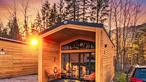 A wooden cabin with a covered porch, a fireplace, and a car parked nearby. - Nice apartment in villa for 5 guests with A/C, TV and terrace (Fischbachau)