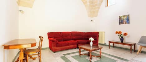 A living room with a red sofa, wooden dining table, and chairs, a coffee table, and a small table with flowers.