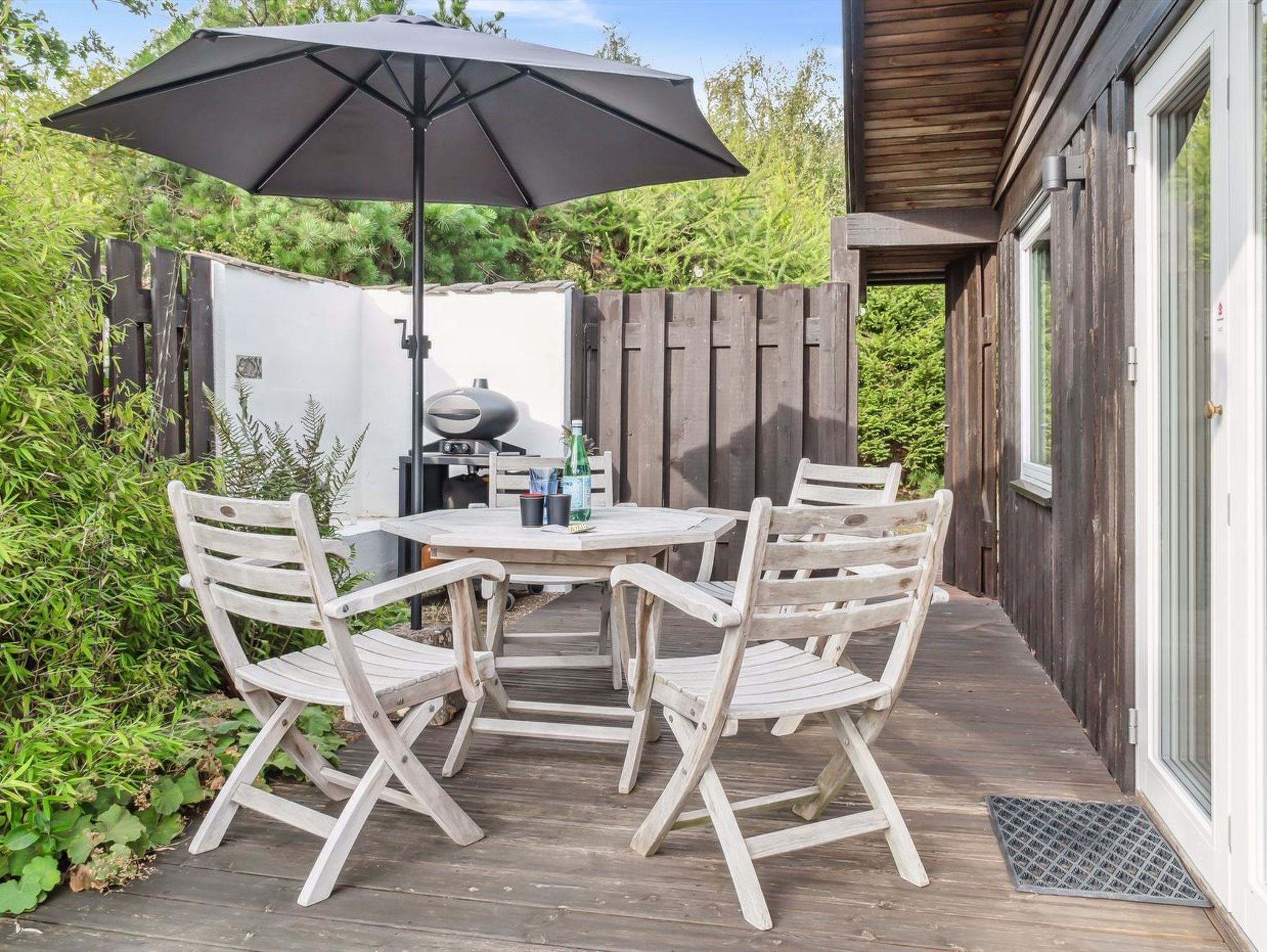 Un patio al aire libre con una mesa, cuatro sillas, una parrilla y un gran paraguas.