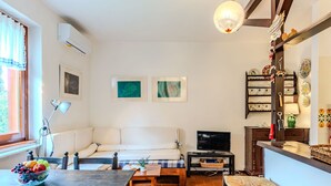 A cozy living room with a sofa, a TV, a dining table with fruit, and a kitchen area with decorative plates. - Lovely apartment for 4 people with WIFI, A/C, TV, patio and pets allowed (Bellano)