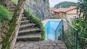 A stone staircase leading to a pool area with a view of a hillside and buildings in the background. - Nice apartment for 8 people with pool and terrace (Torri Del Benaco)