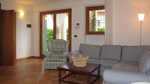 A living room with a striped sofa, a wooden coffee table, a wicker basket, and a chair. There is a door with a light switch and a wall-mounted light. - Nice apartment for 8 people with pool and terrace (Torri Del Benaco)