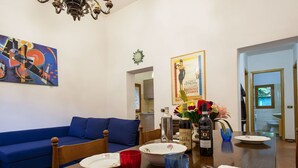 Een eetgedeelte met een houten tafel gedekt voor twee personen, een blauwe bank en een schilderij aan de muur.