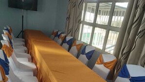 Ein Konferenzraum mit einem langen Tisch, der mit orangefarbenem Tuch bedeckt ist, umgeben von weißen Stühlen mit blau-orangenen Bändern.