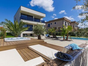 A modern outdoor pool area with lounge chairs, a hot tub, and a wooden deck.