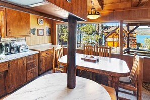 A wooden interior with a kitchen, dining area, and large windows overlooking a lake.