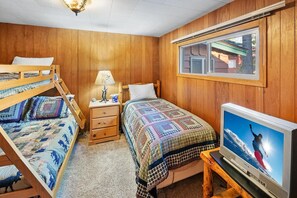 A room with a bunk bed, a single bed, a bedside table with a lamp, a television, and a window. - Walking Distance to Village & Big Bear Marina! Lake Views! Hot Tub! Central A/C! (Big Bear Lake)