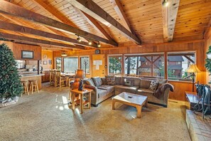 A cozy cabin interior with a wooden ceiling, a living area with a sofa and coffee table, and a kitchen area with a bar.