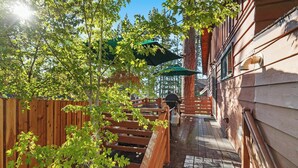 Um deck de madeira com churrasqueira, cerca de madeira e uma casa com telhado verde.