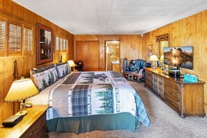 A room with a large bed, wooden walls, a dresser, a television, and a mirror.