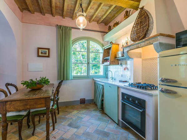 A kitchen with a wooden table, chairs, a window with curtains, a stove, and a refrigerator.