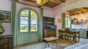 Una habitació acollidora amb sostre de fusta, una finestra gran d'arc i taula de dinar amb caires, i una zona de cuina amb un rentaplat i prestatges.