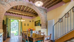 Un comedor con una mesa y sillas de madera, un jarrón de flores y una escalera que sube a otro nivel.