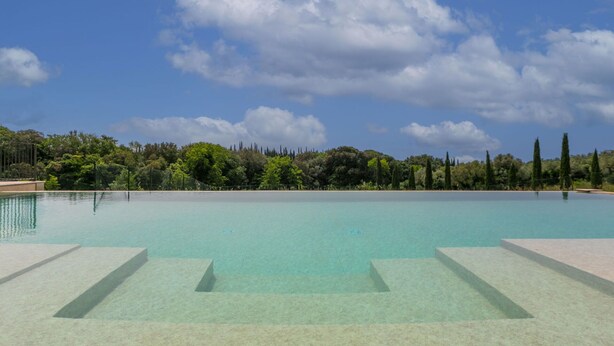 Piscina cristalina con escalones de acceso, rodeada de árboles y un cielo despejado.