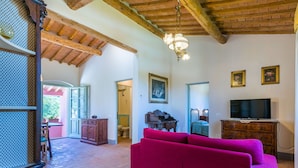 A spacious living area with a red sofa, wooden furniture, a television, and a chandelier. - Beautiful apartment for 4 people with pool, A/C, WIFI, TV, patio, pets allowed and panoramic view (Rosignano Marittimo)