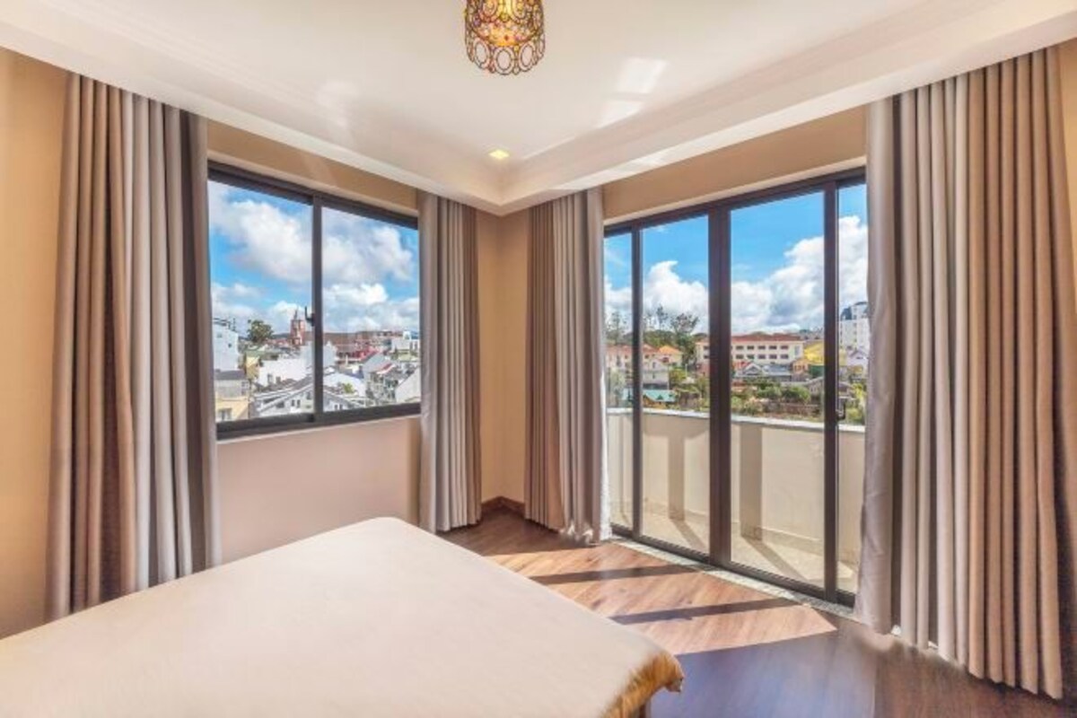 A hotel room with a large bed, a balcony with a city view, and a chandelier.