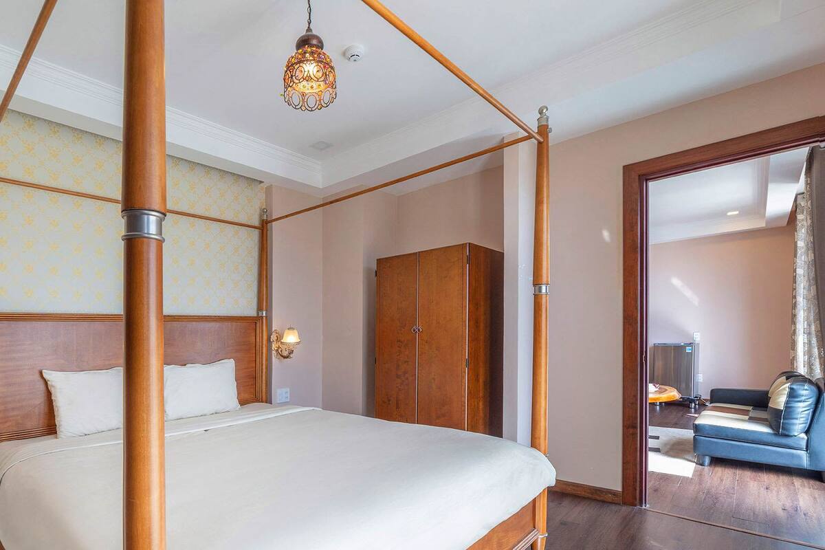 Una cama con dosel, un cabecero de madera, un armario y una zona de estar con sofá y mesa de centro.