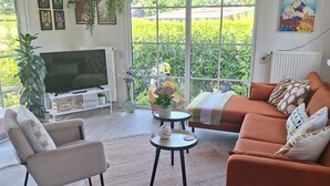 A living room with a sofa, armchair, TV, and a large window with a view of greenery. - Private Sanctuary/Zen Den/nature lovers (Voorthuizen)