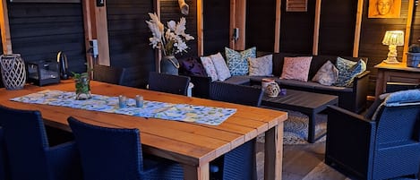 Un espace de détente intérieur accueillant, avec une table et des chaises en bois, un canapé agrémenté de coussins à motifs et une horloge fixée au mur.