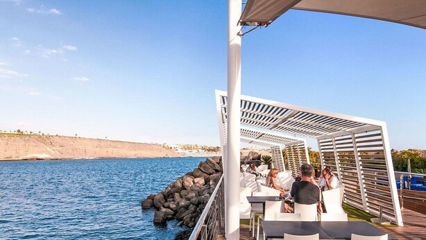Une terrasse avec des sièges extérieurs donnant sur une étendue d’eau, avec une côte rocheuse en arrière-plan.