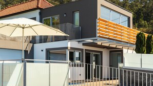Une maison moderne à deux étages, dotée d’un balcon, d’une piscine et d’un patio couvert.