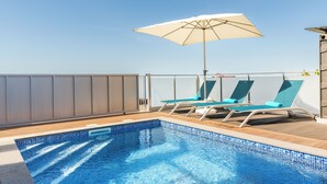 Une piscine sur le toit, avec deux chaises longues et un grand parasol.