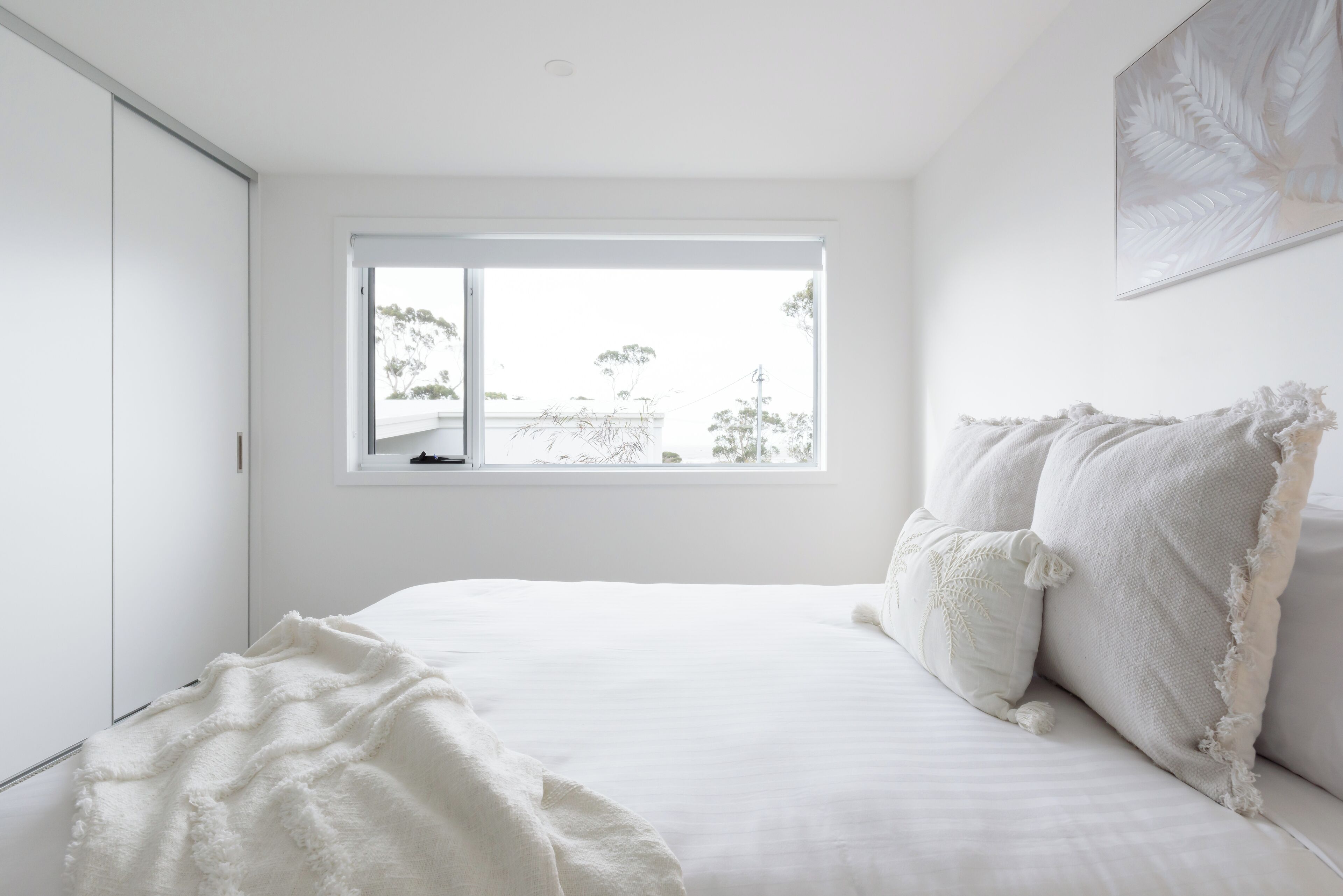 A bedroom with a large window, a bed with white bedding, and a view of trees outside.