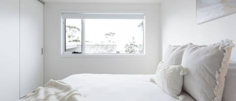 A bedroom with a large window, a bed with white bedding, and a view of trees outside.