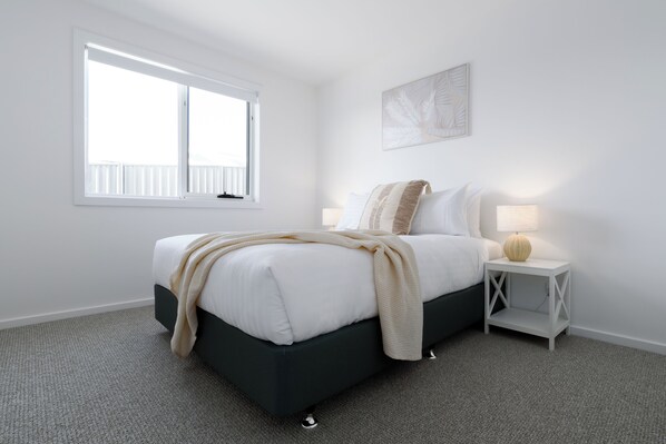 A bedroom with a bed, a bedside table with a lamp, a window, and a wall-mounted artwork. - Bright & Airy Coastal abode (Bridport)