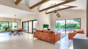 A spacious living area with a large sofa, a dining table, and a pool view.