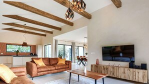A spacious living room with a large sofa, a coffee table, and a TV mounted on the wall.