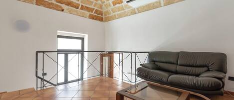 A spacious living area with a leather sofa, a glass coffee table, and a view through a glass door to a balcony.