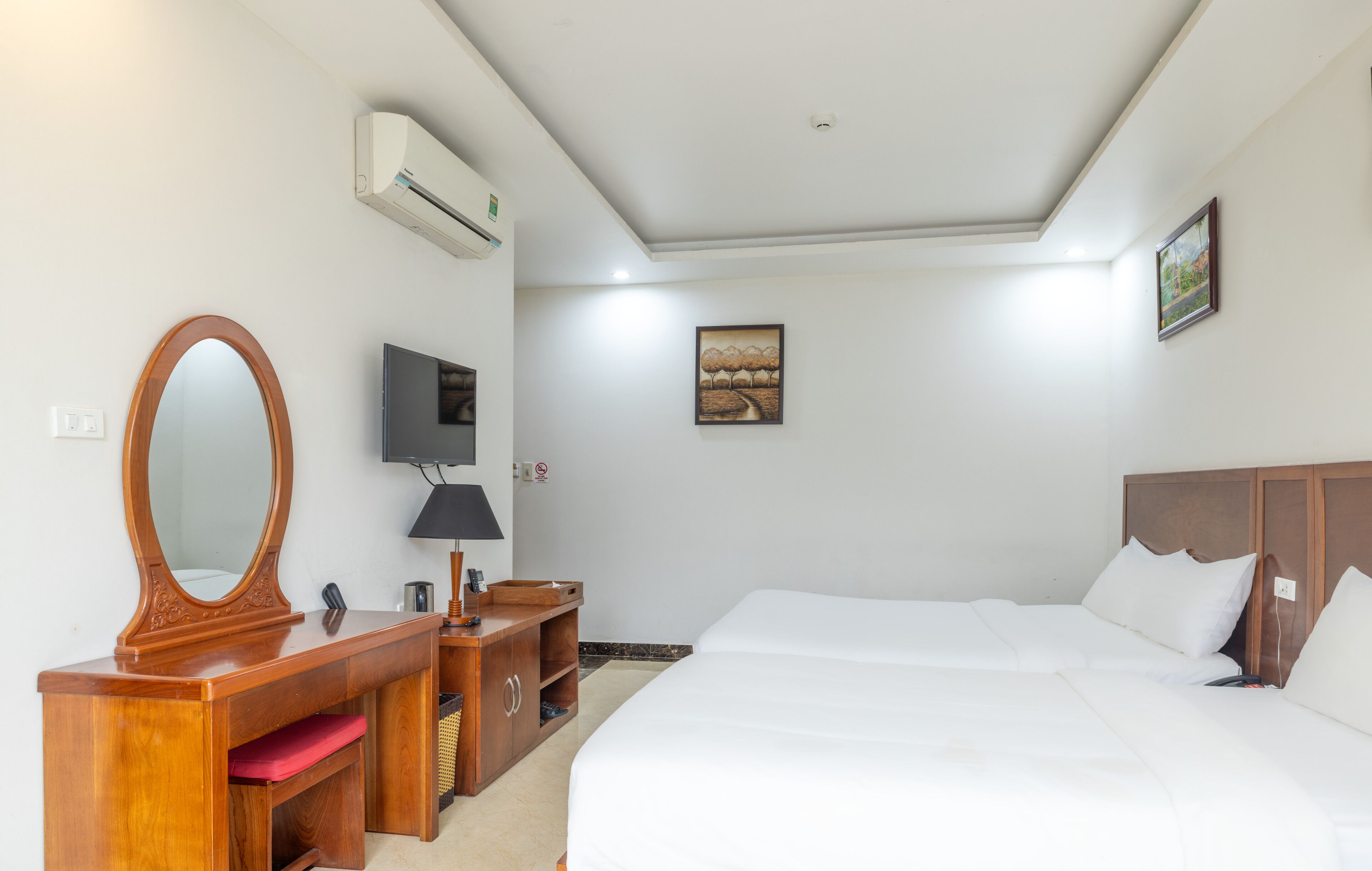 A hotel room with a wooden dresser, a large mirror, a flat-screen TV, a bed with white linens, and a painting on the wall.