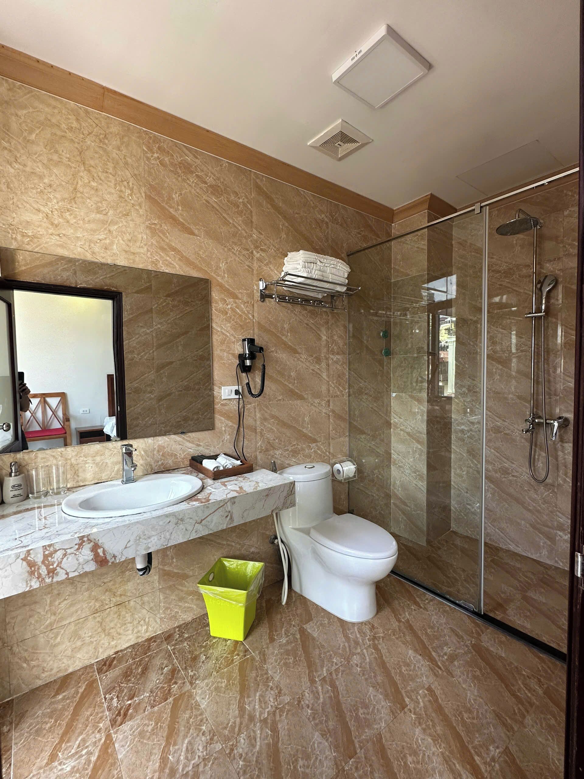 A modern bathroom with two sinks, a toilet, a glass shower enclosure, and a marble-tiled floor.