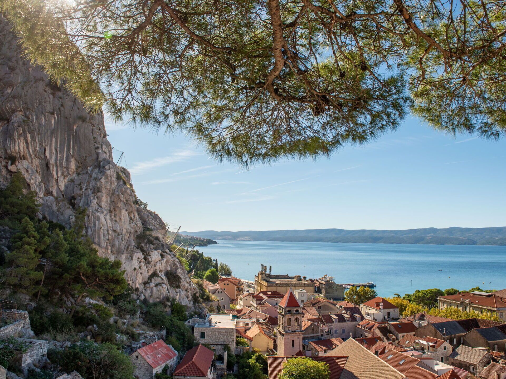 A coastal town with historic buildings, a prominent church tower, and a rocky cliff overlooking the sea.