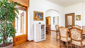 A spacious living room with wooden flooring, a large potted plant, a white cabinet, and a dining area with floral upholstered chairs. - Stunning private villa for 11 guests with WIFI, TV, balcony and pets allowed (Arizzano)