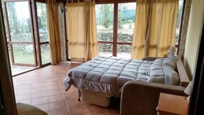 Une chambre avec un grand lit, une table de chevet en bois et une vue sur un jardin, visible à travers une porte vitrée.