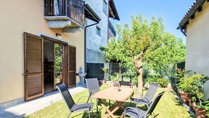 En udendørs terrasse med et træbord og stole, omgivet af en velholdt græsplæne og plantekasser.