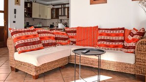 En hyggelig stue med en sofa i flet, et lille rundt bord og et køkken i baggrunden.