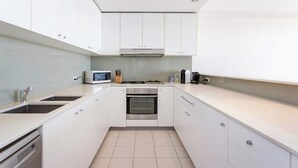 A modern kitchen with white cabinets, a built-in oven, a microwave, and a gas stove. - “Enjoy Fremantle from this spacious 3BR apartment with port views, communal pool & free parking — walk to Rottnest Ferry & Markets.” (Fremantle)
