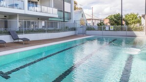 A swimming pool with a wooden deck and lounge chairs. - “Enjoy Fremantle from this spacious 3BR apartment with port views, communal pool & free parking — walk to Rottnest Ferry & Markets.” (Fremantle)