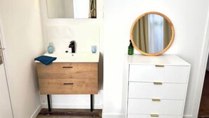 A bathroom with a wooden vanity, a white cabinet with gold handles, a round mirror, and a blue towel. - La Suite Private Spa Blue in the heart of Douai (Douai)