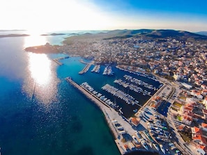 An aerial view of a coastal town with a marina, residential buildings, and a clear sky.