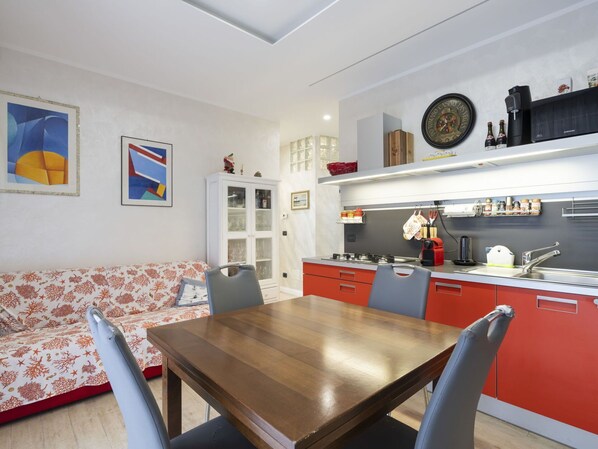A modern kitchen with a dining area, featuring a wooden table, red cabinets, and a white cabinet with glass doors.