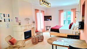 A cozy living room with a fireplace, a television, a dining table with chairs, and a bed with a red blanket. - RANDOM LISTING (Sainte-Tulle)