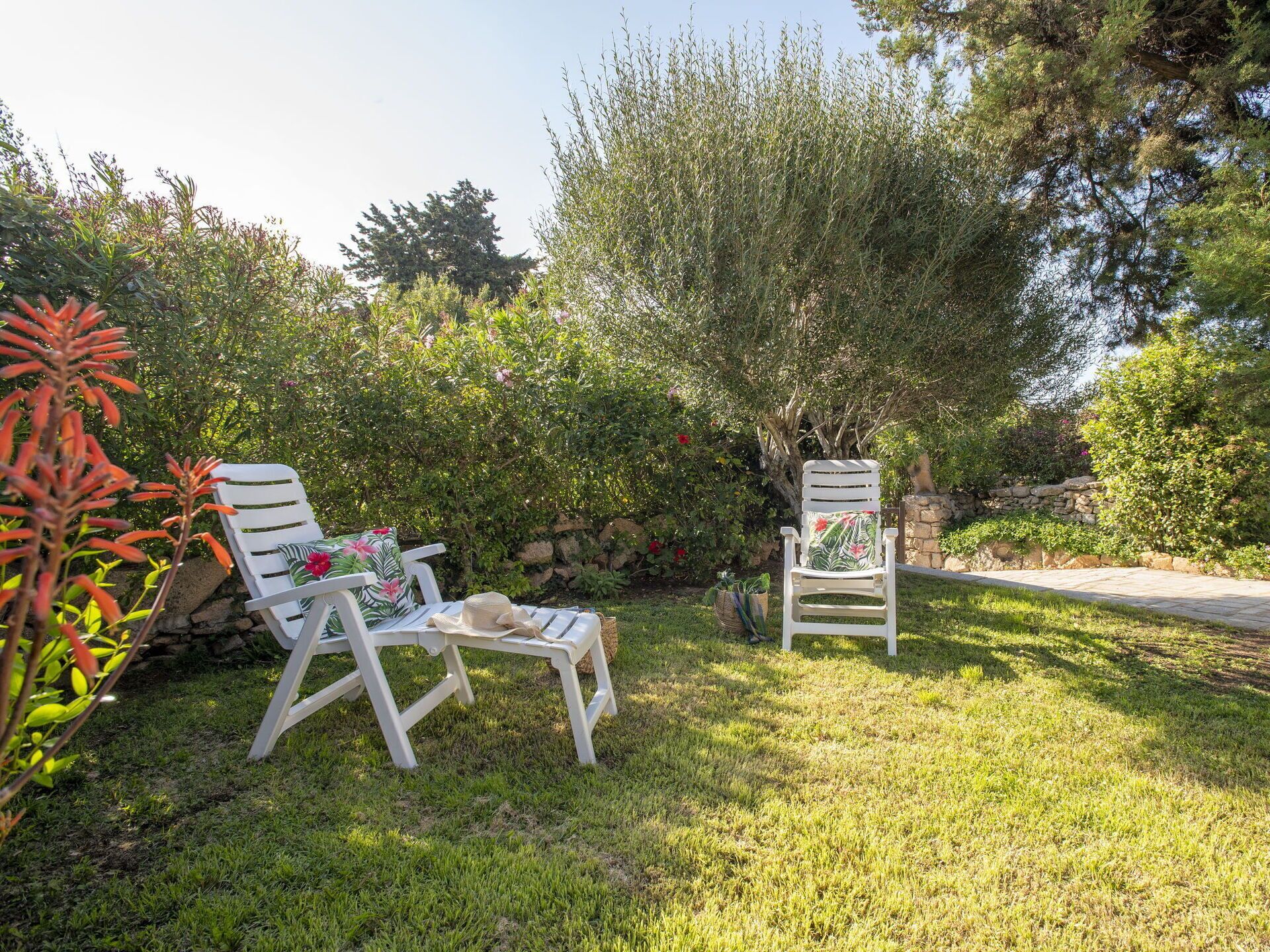 Deux fauteuils de jardin blancs, dotés de coussins à motifs floraux, dans un cadre verdoyant et luxuriant.