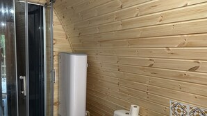 Une salle de bain rustique, aménagée dans une cabane en bois, avec douche, toilettes et lavabo.